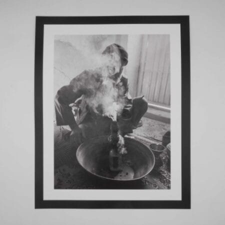 Black and white image of an Afghan man smoking hash through a traditional hookah