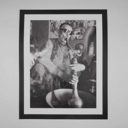 Black and white image of an Afghan man smoking hash through a traditional hookah