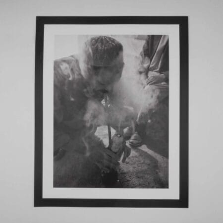 Black and white image of an Afghan man smoking hash through a traditional hookah
